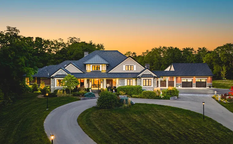 Custom transitional luxury home in Burlington Ontario with a long winding driveway, manicured lawn, and beautiful evening sunset lighting